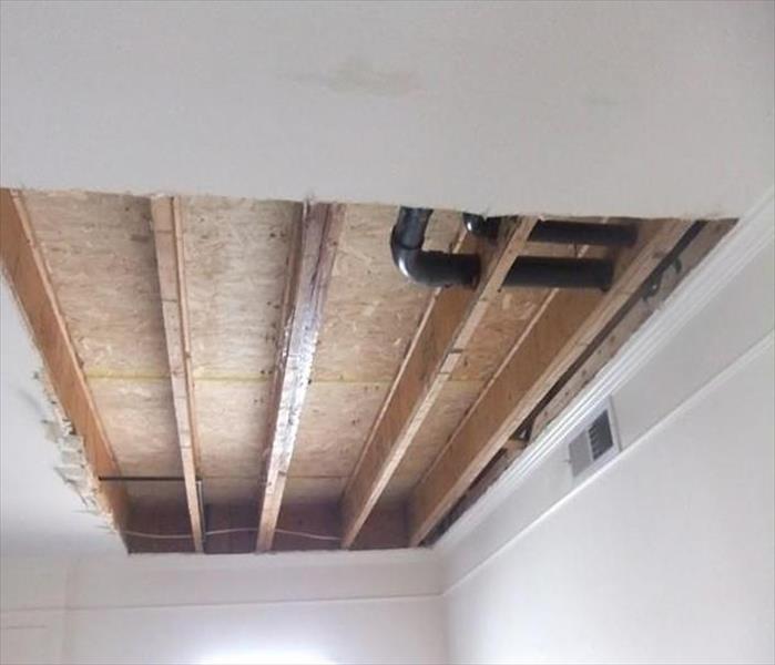 cut out ceiling section showing subfloor and black plumbing